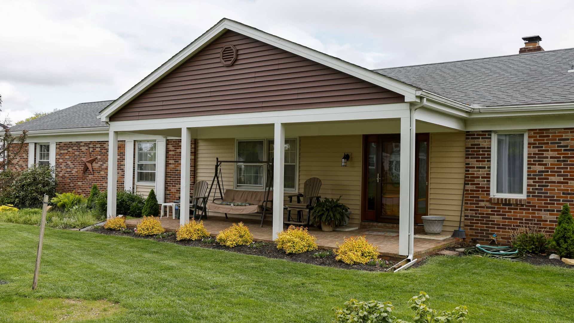 ranch style brick home with a frame roof over a back porch area that has gliders and furniture on it